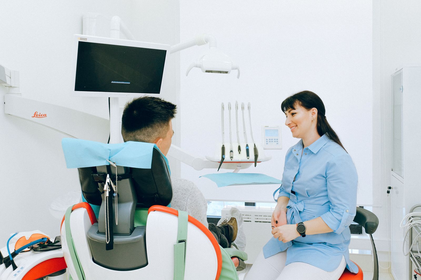 Dentista conversando con un paciente sentado en el sillón de una clínica dental luminosa
