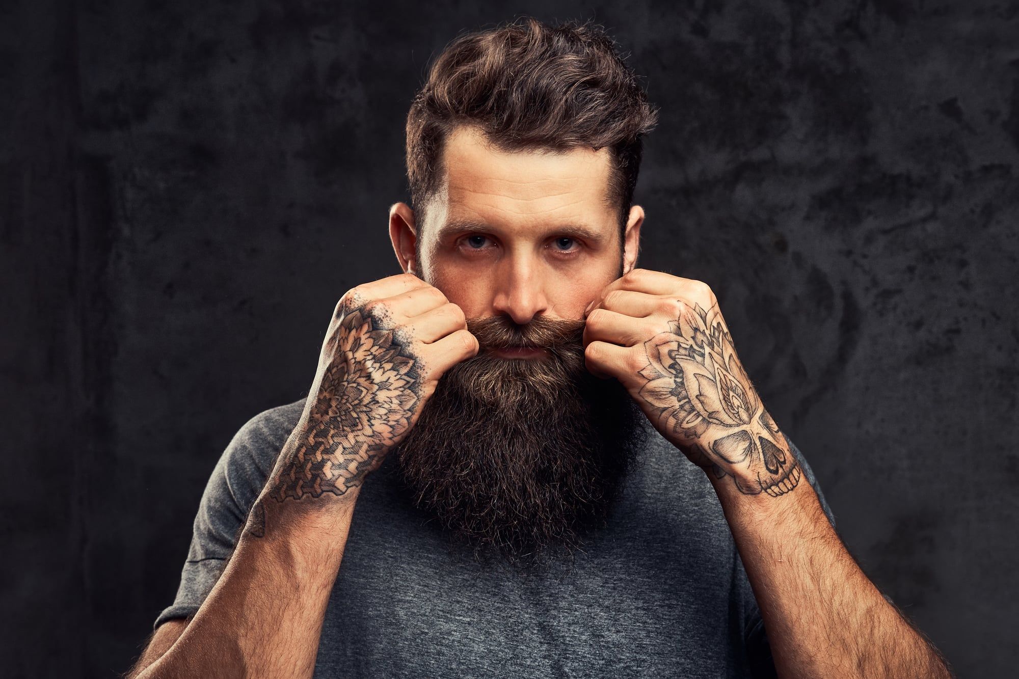 Hombre con barba poblada y manos tatuadas atusándose el bigote