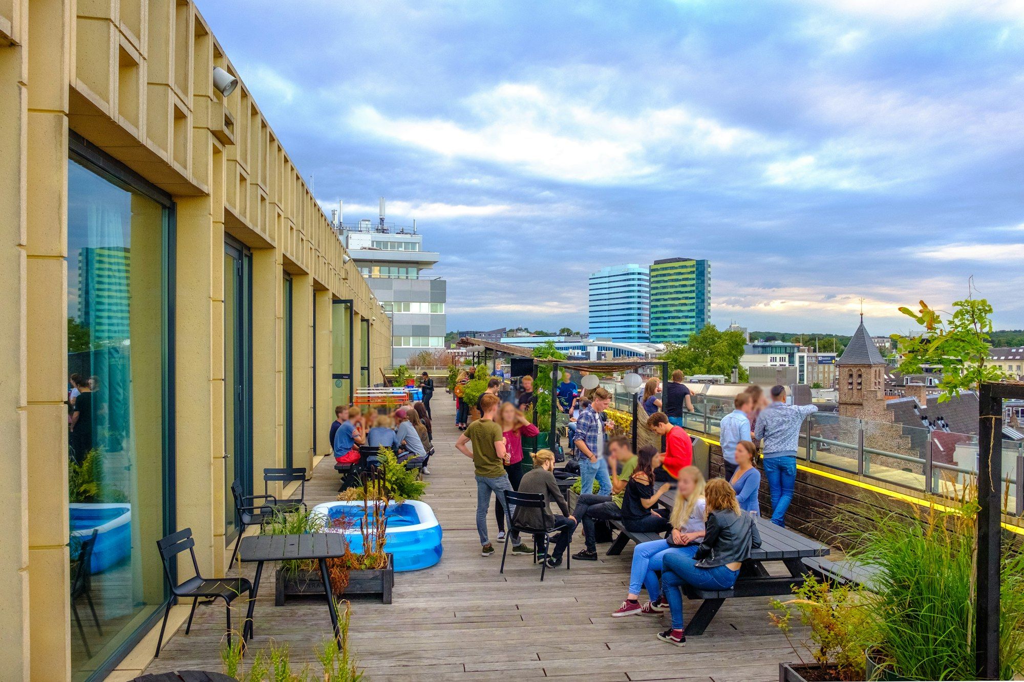Terraza de un ático en la ciudad con jardineras, tarima y gente charlando al atardecer